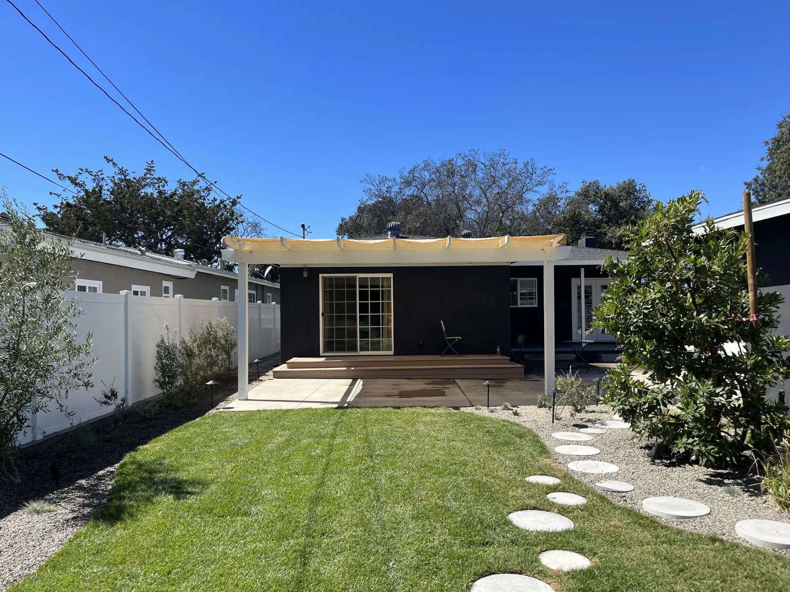 A backyard lawn with concrete stepping stones leading to a modern house with a wooden pergola.