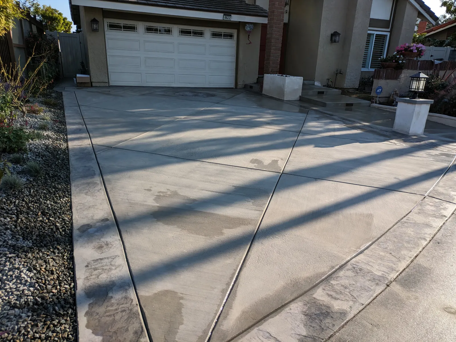 A concrete driveway with decorative diagonal joint lines leads to a house with a garage door.