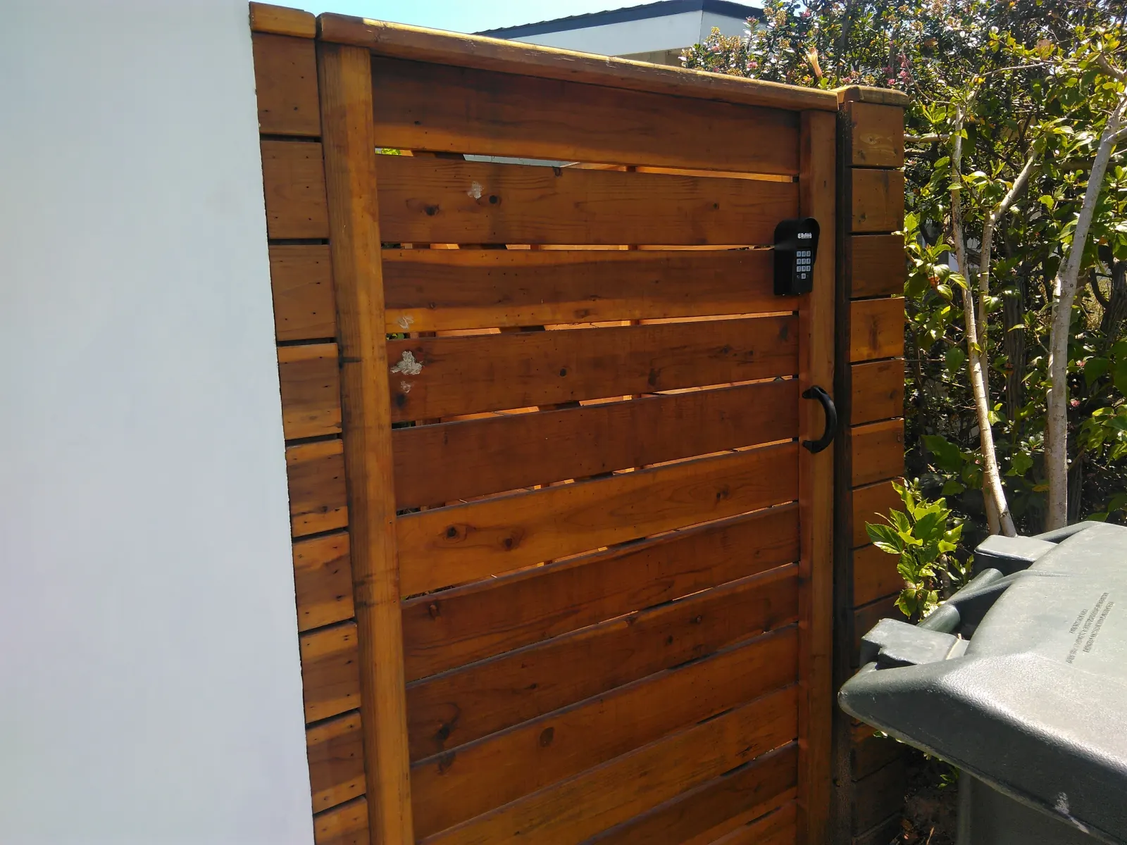 A horizontal wood slat gate with black hardware mounted next to a clean white wall.