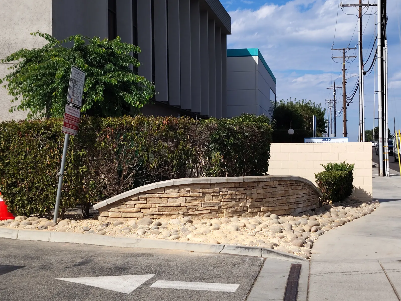 A curved low stacked-stone retaining wall surrounding a gravel garden bed near a street curb.