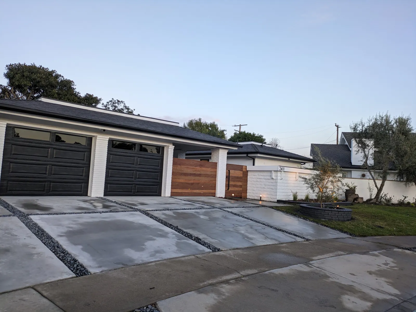 A modern concrete driveway with strip gravel joints leading to a three-car garage with black doors.