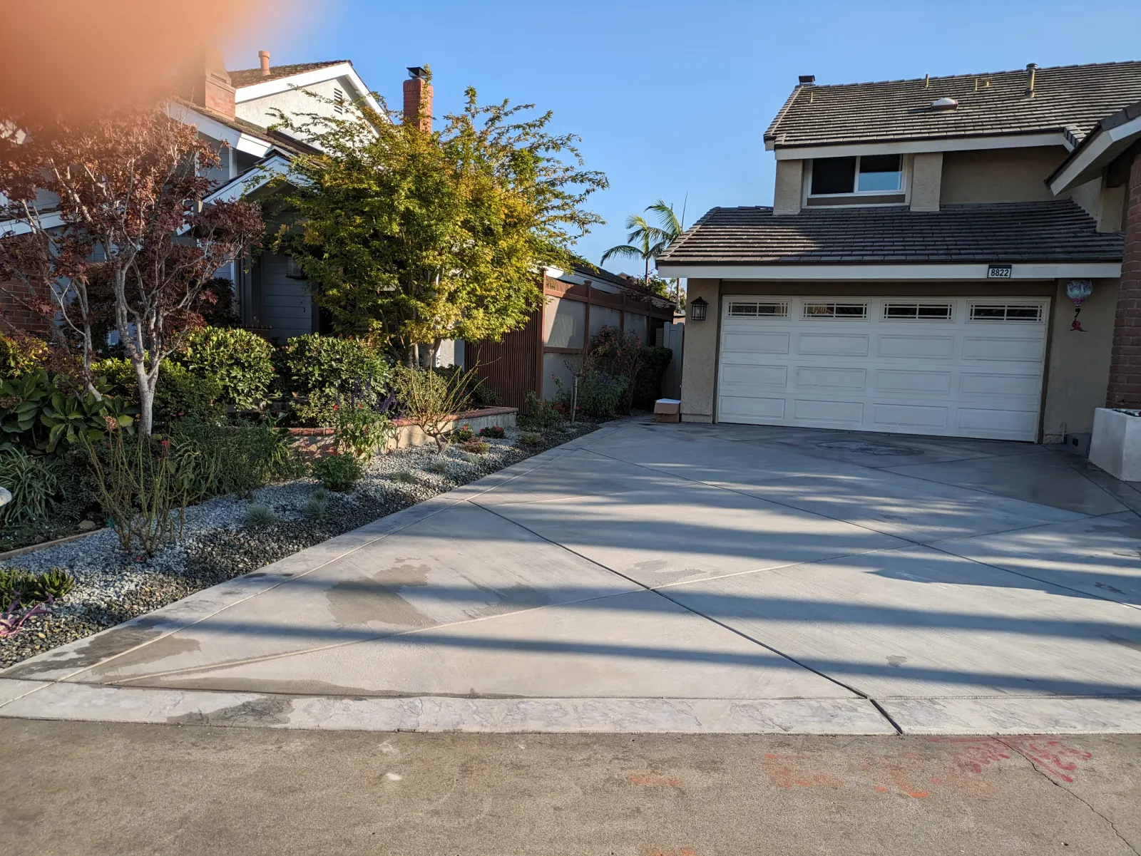 Wide view of a concrete driveway leading to a house garage, with landscaped beds on the left.