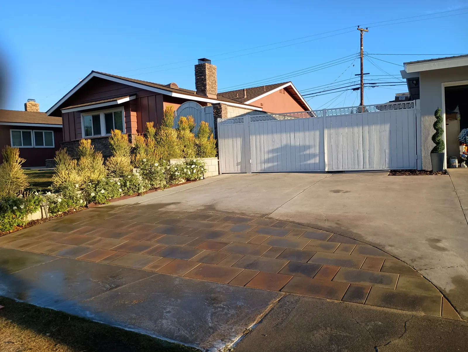 A paved driveway apron in front of a white gate and fence of a residential home.