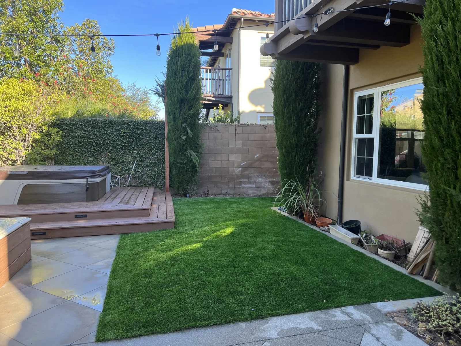 A small, manicured green lawn in a backyard next to a residential building and a wooden deck.