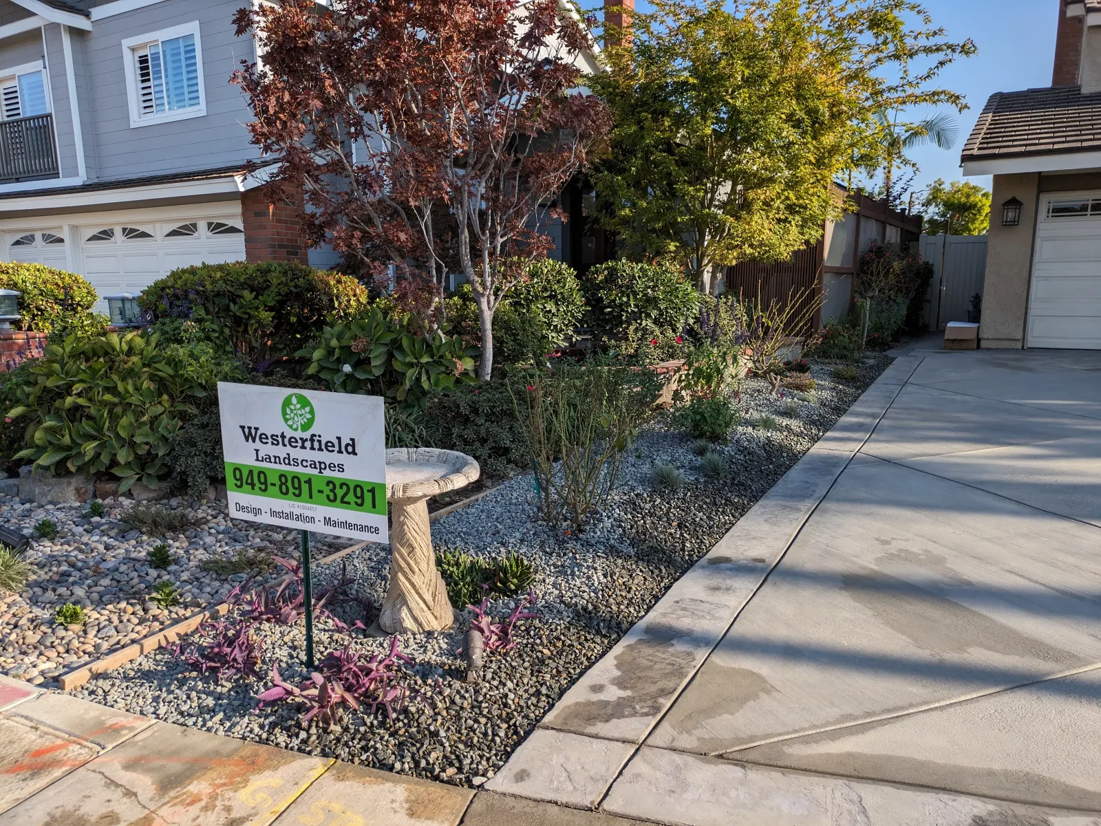 Front yard landscaping with gray gravel mulch, decorative plants, birdbath, and a company yard sign.
