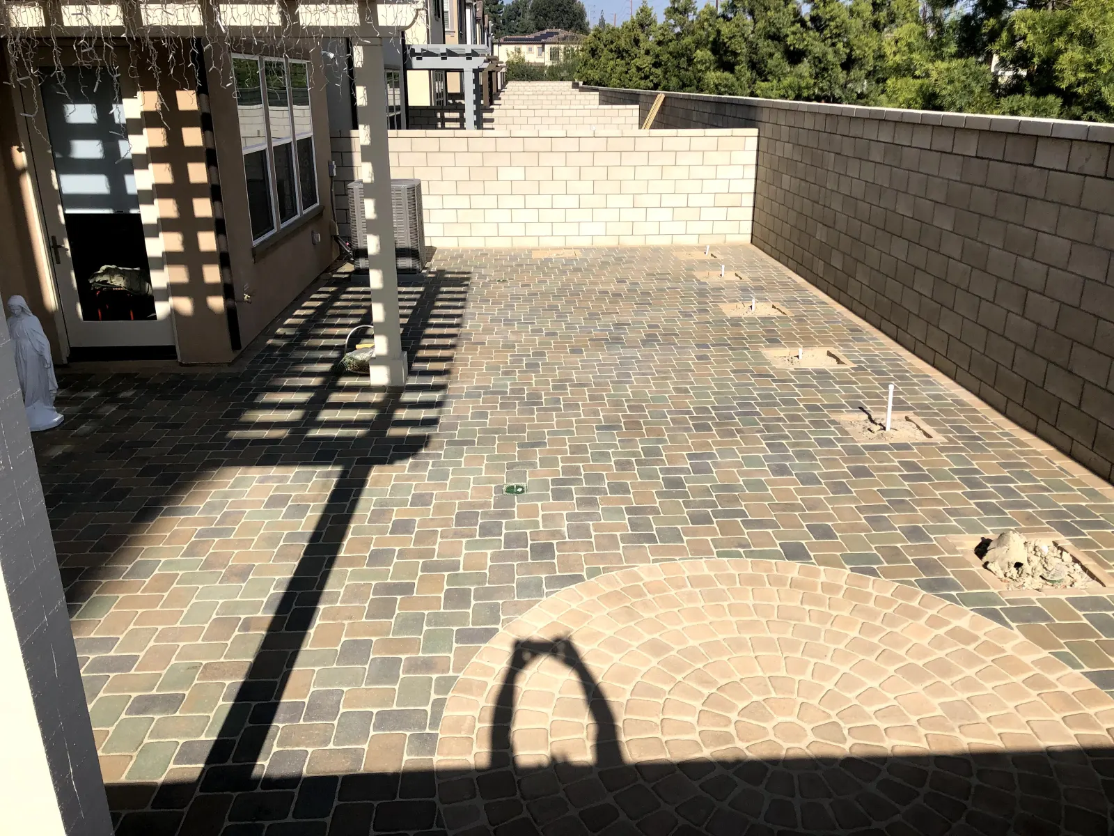 An outdoor patio area covered in interlocking stone pavers beneath a wood timber pergola.