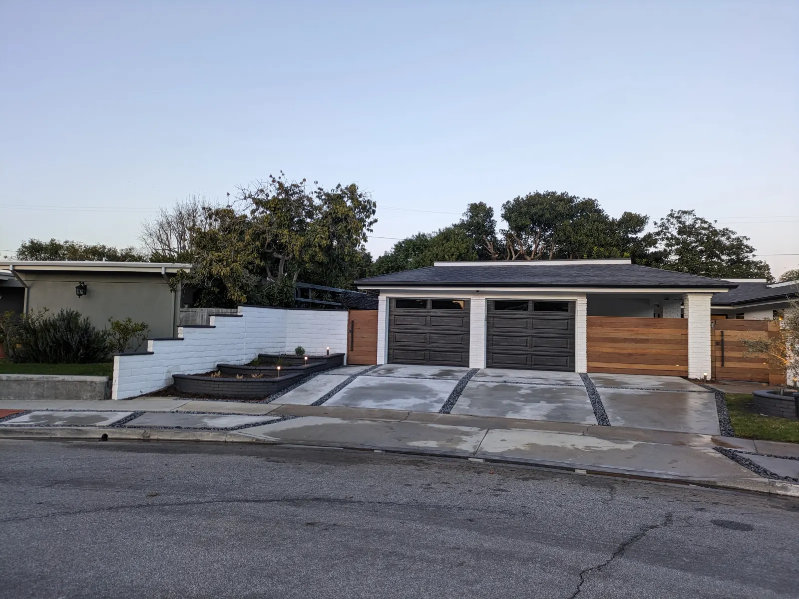 A wide concrete driveway leading to a modern home with dual garage doors and a tiered wall.