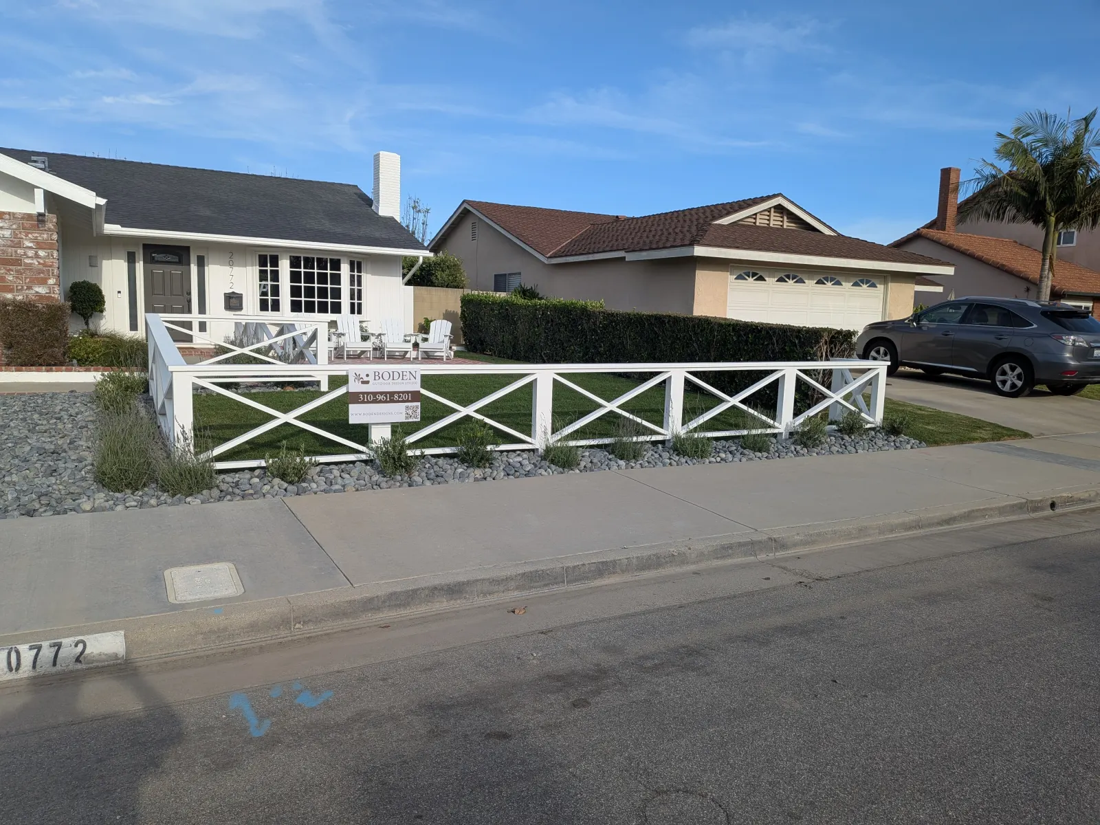 Front yard with a low white decorative cross-buck fence and gravel ground cover next to a street.