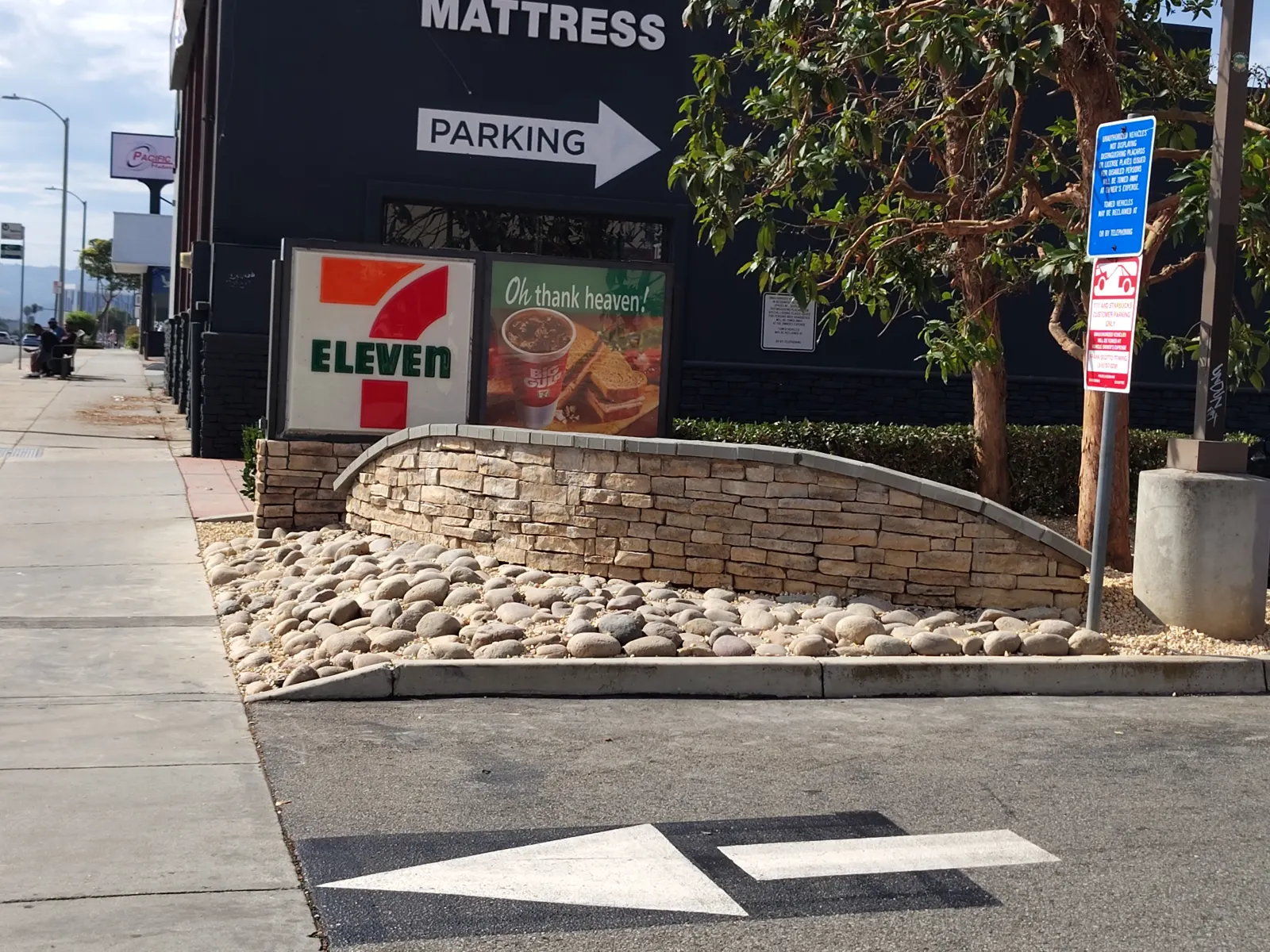 A low stone retaining wall planter filled with large river stones situated in a commercial parking lot.