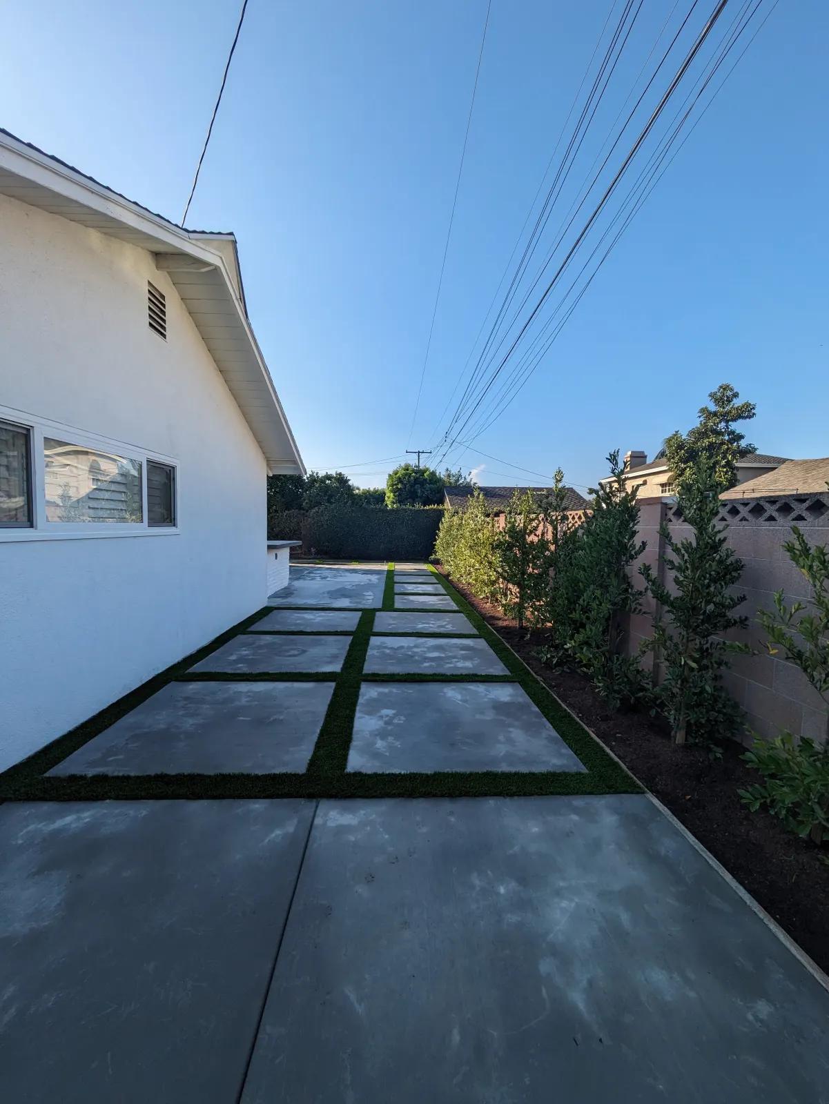Modern driveway design with rectangular concrete pads separated by thin strips of green turf.