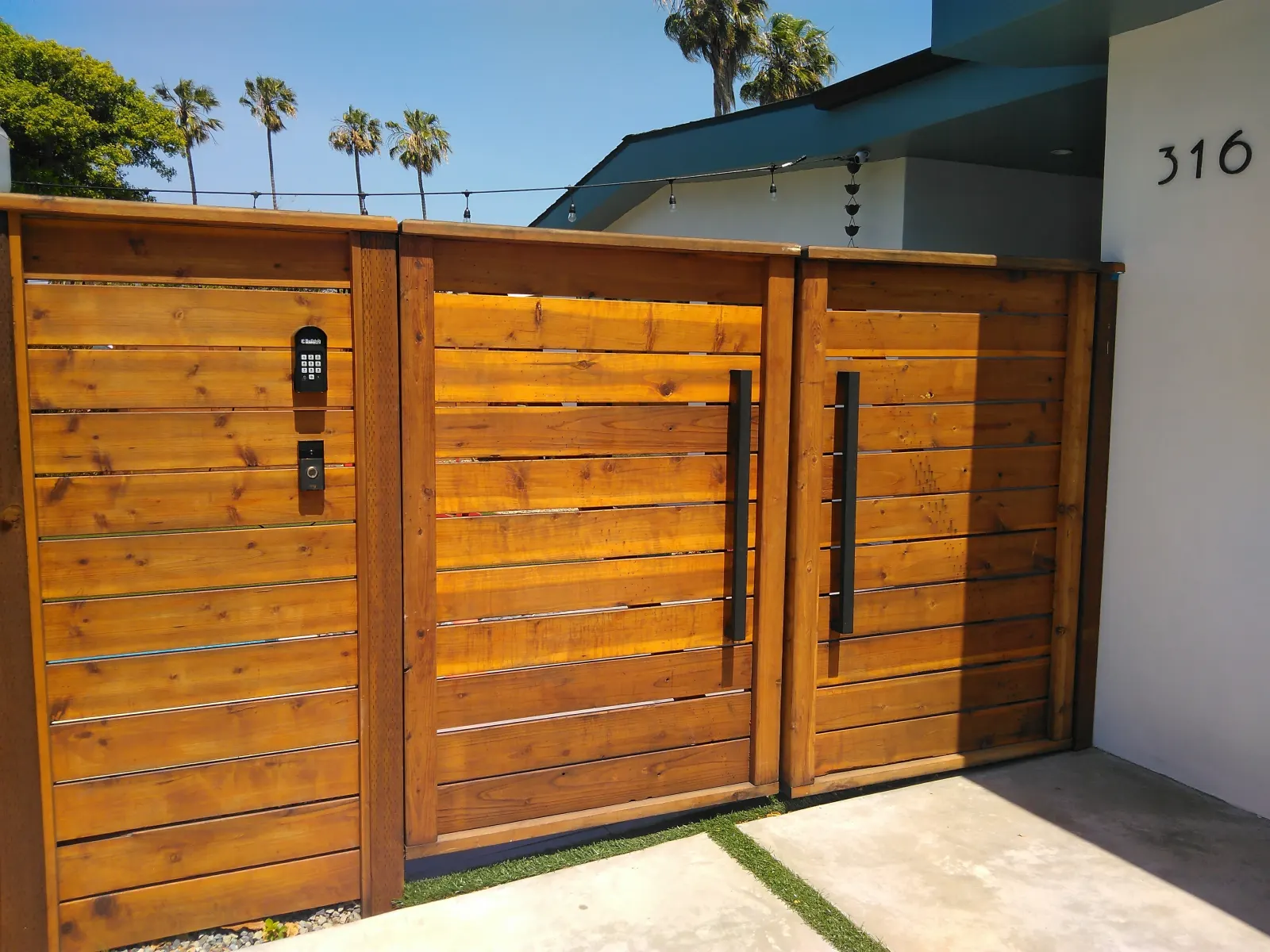 Modern horizontal wood-slatted gate with black metal frames and hardware.