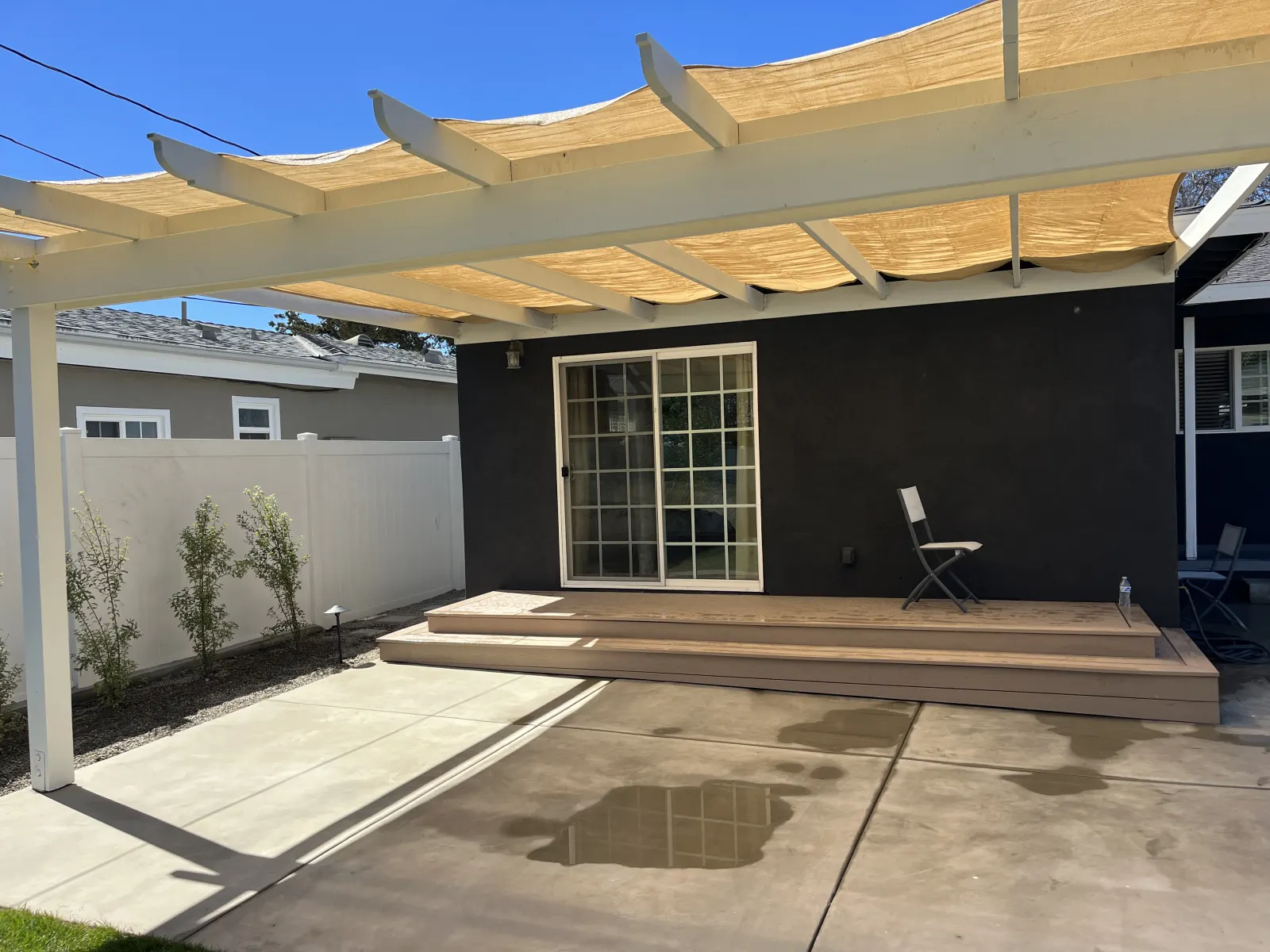 A modern white painted pergola with a canvas shade cover over a concrete back patio.