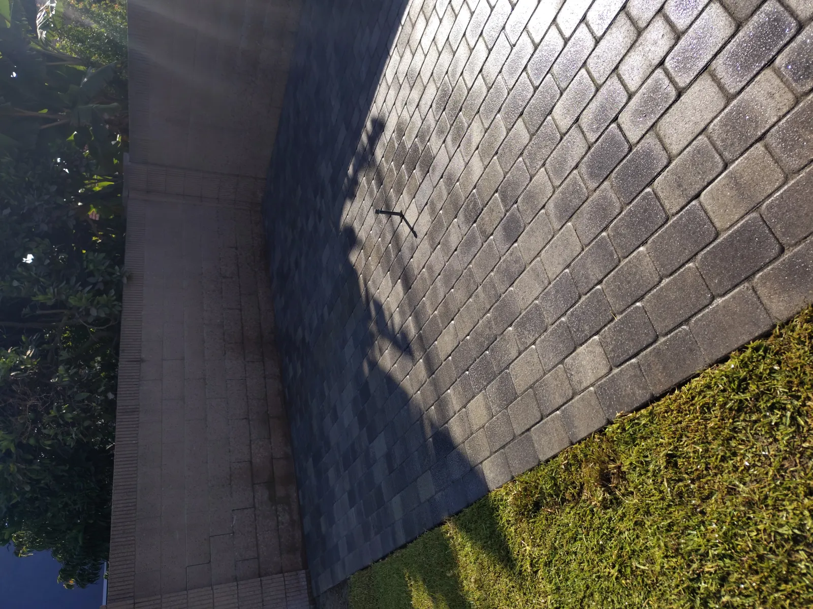 Close-up angled shot showing dark interlocking paving stones bordered by concrete and green grass.