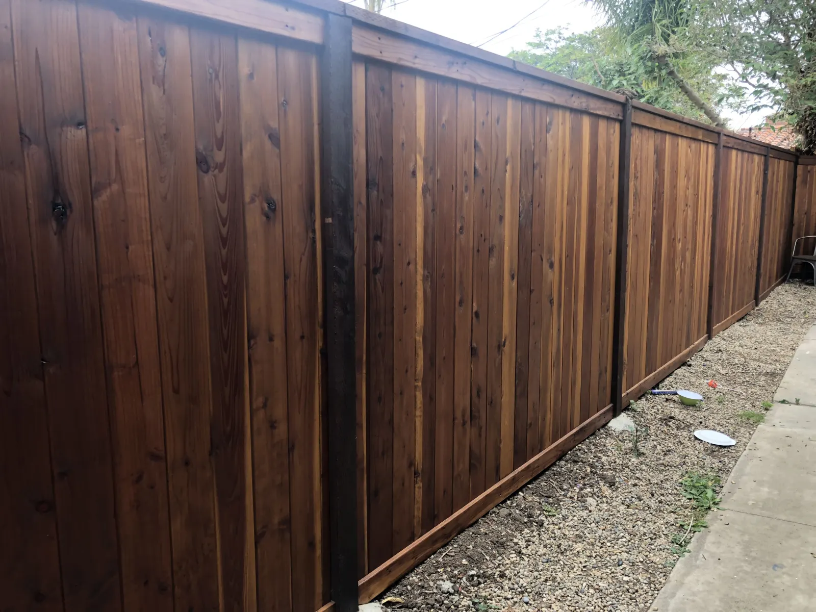 A newly installed dark wood privacy fence with gravel bedding at the base.