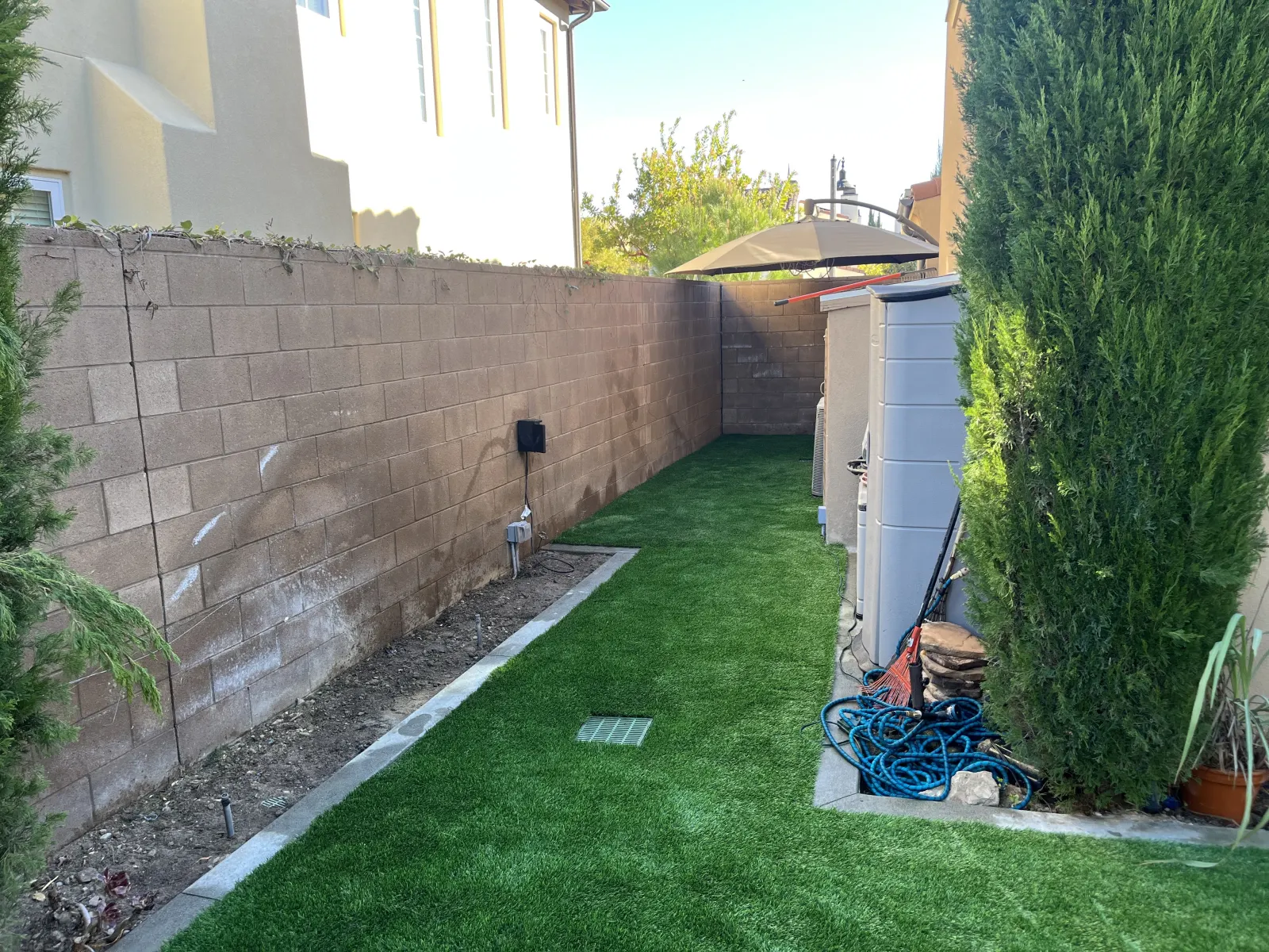 Narrow side yard featuring artificial turf, a tall masonry block wall on the left, and a white storage unit on the right.