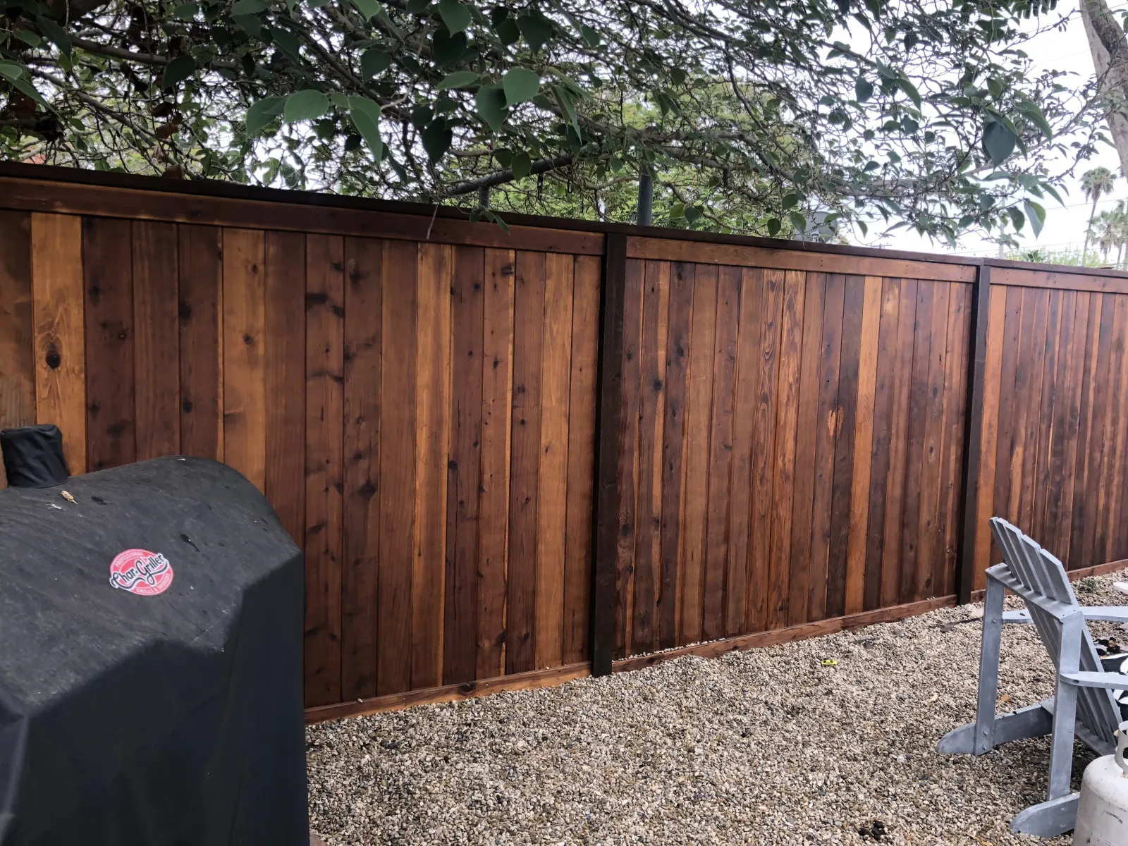 Horizontal wood board fencing with dark metal posts set in front of a gravel surface.